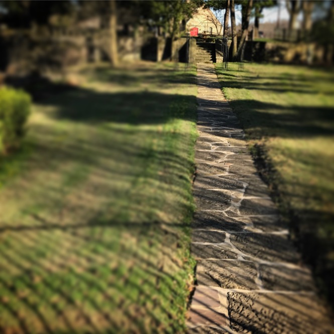A stone path leads between grassy shadows towards a red church door in the distance.